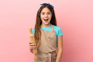 Little caucasian girl holding a rolling pin isolated on pink background with surprise facial expression