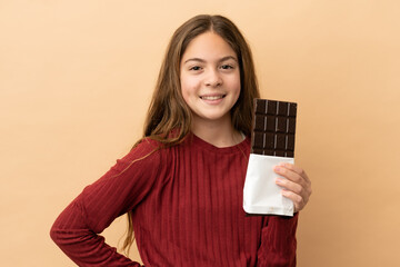 Little caucasian girl isolated on beige background taking a chocolate tablet and happy