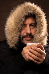 portrait d'un homme de 50 ans qui tient une tasse de thé ou de café fumante dans ses mains pour se réchauffer. Il a froid et il porte un gros manteau d'hiver