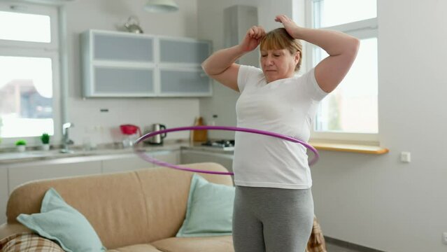 Overweight mature woman in white t-shirt and gray leggings trying to lose weight with hula hoop exercises
