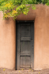Obraz premium Rustic wood door and adobe wall under pear tree in Santa Fe, New Mexico