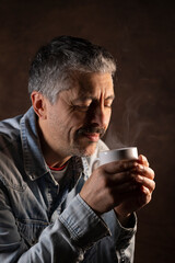 portrait d'un homme qui boit un café ou un thé. Il tient une tasse fumante dans ses mains pour se...