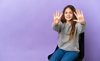 Little caucasian girl sitting on a chair isolated on purple background counting nine with fingers