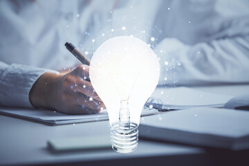 Bulb hologram over hands taking notes background. Concept of idea. Double exposure