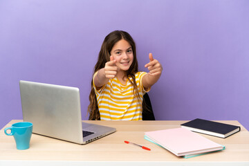 Little student girl in a workplace with a laptop isolated on purple background pointing front with happy expression