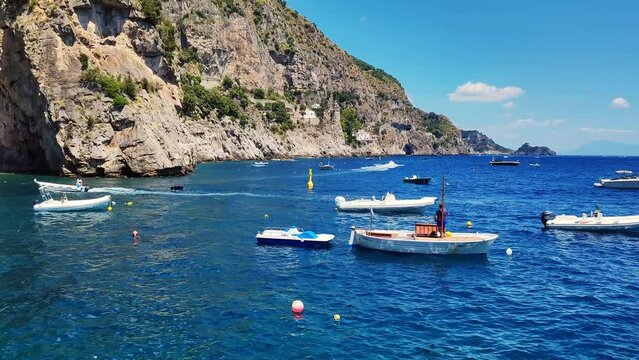 Boats floating in the Amalfi coast sea. Looking from the port to the open sea. Rowboat, fishing boats and yachts on a sea. Blue transparent water with cliffy shore. Rocky cliffs, floating boats.
