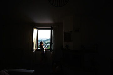 Girl stand and looking from window in sunset.