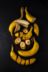 ripe fresh sliced and whole banaras on a clay plate and on a black background. top view. dark artistic vertical photo