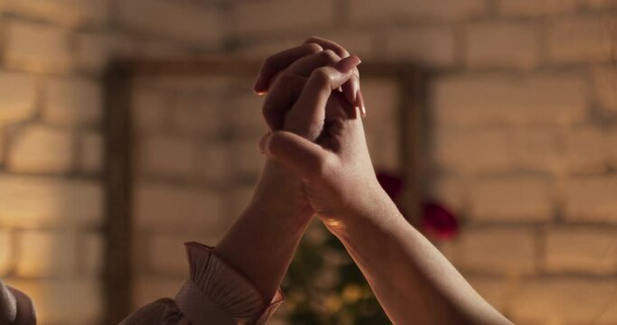 Two female hands lovingly join and hold each other in the romantic atmosphere of the interior.