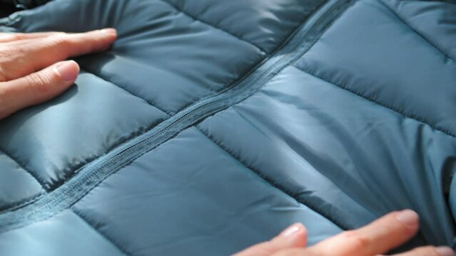 Female hands touching groping material emerald green waterproof fabric of winter jacket, down jacket. Textile, clothing production, autumn bright jacket. Fashion, Style. Clothes background
