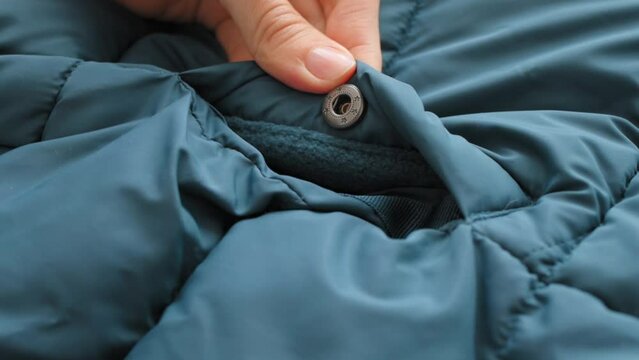 Close-up of female hands touches pocket of green winter emerald jacket with metal button, down jacket. Details of an autumn waterproof jacket. Textile, material, Fashion, Style