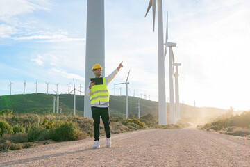 Worker with a tablet points and looks toward renewable energy windmills