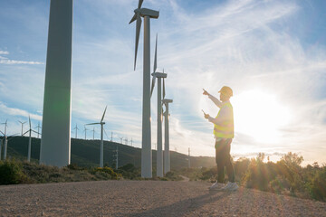 Unrecognizable male worker points at wind turbines at sunset