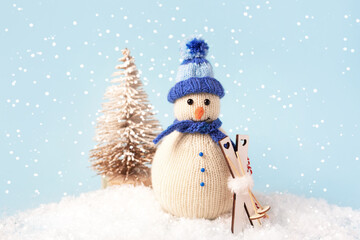 Christmas composition of a knitted snowman in a blue hat and scarf with skis on the background of a small Christmas tree