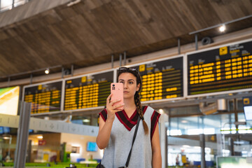 Woman at the airport looks at her boarding pass on her smartphone to check departure time.