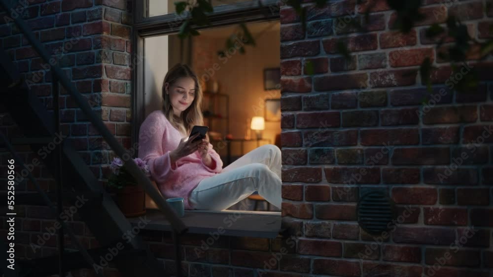 Aufkleber beautiful white woman using smartphone while sitting on an open windowsill. attractive girl with hea