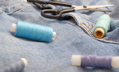 Sewing accessories. Multicolored threads, scissors, denim. Selective focus. The concept of hobby, repair and tailoring.