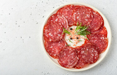 Slices of salami sausage served on a round plate with rosemary and pink salt. Overhead shot.