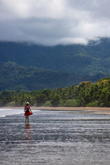 a lone girl with a backpack walks on a paradise tropical beach in marino ballena national park, Costa Rica; a panorama of a Costa Rican beach with palm trees and mountains in the background