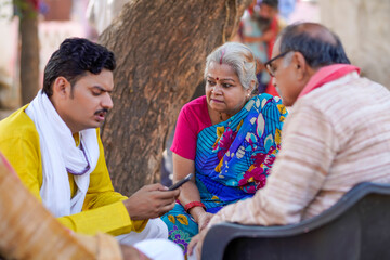 Indian farmer using smartphone and discussing with his parents