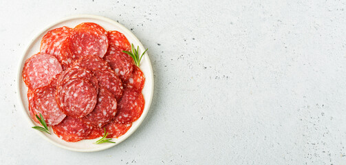 Sliced salami sausage on a plate over white background with space for text