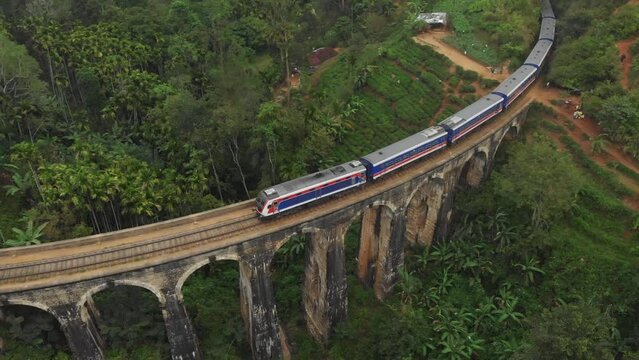 Train crossing the Nine Arches Bridge in Sri Lanka (Ella) surrounded by lush green landscape, tea plantations and rolling hills. Drone footage 4K.
