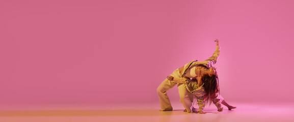 Modern dance art. Young girls, couple of dancers in sports style clothes dancing experimental dances isolated over light pink background in neon. Concept of music, emotions, dance