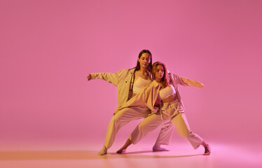Two stylish female dancers in casual style clothes dancing contemporary choreography dance over crystal pink background. Concept of modern art, creativity, fusion