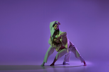 Dance performance. Stylish female dancers at contemporary choreography dance class isolated over crystal purple background. Style, youth, music and fashion