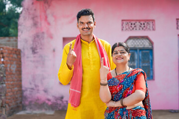 Indian rural couple showing voting sign with finger at home