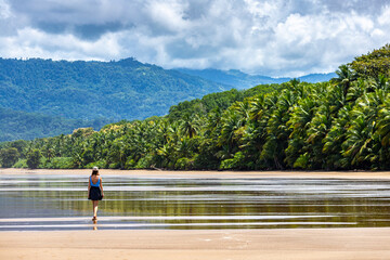 a lone beautiful girl in a skirt walks along a tropical beach with palm trees in marino ballena...