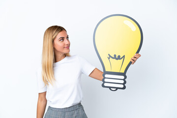 Blonde Uruguayan girl isolated on white background holding a bulb icon with happy expression