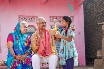 Fototapeta na wymiar Indian little girl holding winning trophy with grandparents