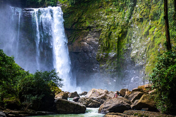 beautiful girl in pink bikini sits on rocks below eco chontales waterfall in Costa Rica; powerful waterfall in rainforest in Costa Rica