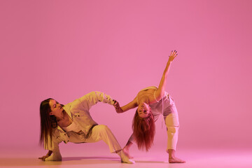 Two stylish female dancers in casual style clothes dancing contemporary choreography dance over crystal pink background. Concept of modern art, creativity, fusion