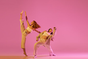 Modern dance art. Young girls, couple of dancers in sports style clothes dancing experimental dances isolated over light pink background in neon. Concept of music, emotions, dance