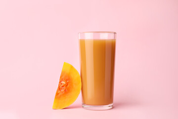 Tasty pumpkin juice in glass and cut pumpkin on pink background