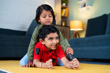 Young siblings kids fighting for remote control while watching tv or television at home - concept...