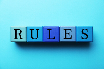 Word Rules made of wooden cubes with letters on light blue background, flat lay