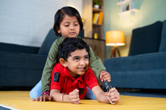 Young siblings kids fighting for remote control while watching tv or television at home - concept of childhood lifestyle, siblings quarrel and technology.