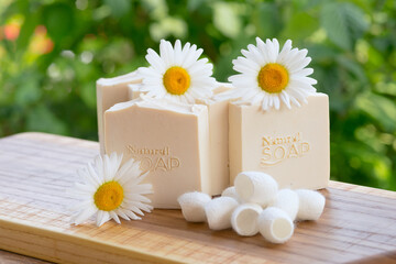 White handmade soap with chamomile flowers and silk cocoons on a green background