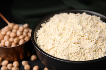 Chickpea flour in bowl and seeds on black table, closeup