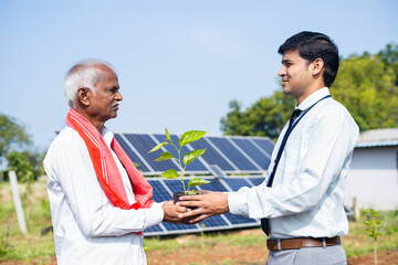Engineer giving plant to farmer in front of solar power plant at farmland - concept of encouraging use renewable energy, save tress and sustainable lifestyle