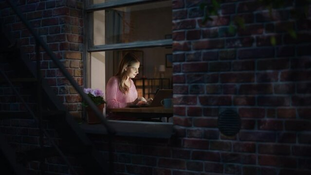 White Woman Using Laptop while Sitting at her Desk in a Cosy Apartment. Young Female Freelance Finances Consultant Sending Emails and Answering Customers While Working from Home at Night.