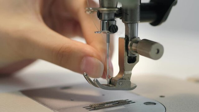 Woman sews grey fabric on a professional sewing machine while sitting at her working place in fashion workshop.The seamstress's hands hold textiles for the production of clothes.Designer sew the dress