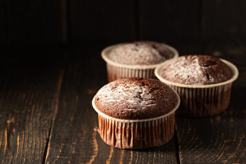 Chocolate muffins with powdered sugar on a black background. Still life close up. Dark moody. Food photo.