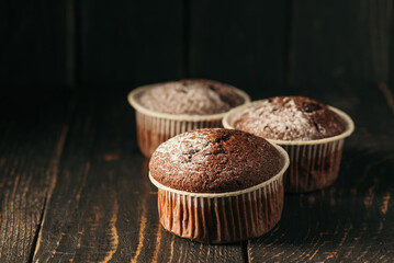 Chocolate muffins with powdered sugar on a black background. Still life close up. Dark moody. Food photo.