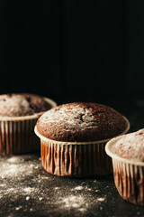 Chocolate muffins with powdered sugar on a black background. Still life close up. Dark moody. Food photo.