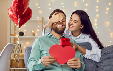 Joyful young couple celebrating St Valentine's Day. Loving woman makes surprise for her boyfriend...