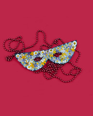 The masquerade mask is decorated with dried pressed flowers and a festive garland of beads lies on a magenta background. Color of the year.